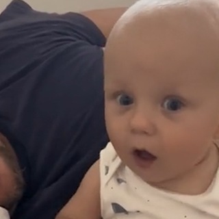 Ein kleines Baby sitzt neben dem schnarchenden Papa und wundert sich lustig über die Geräusche. (Foto: TikTok @zape007 (Screenshot))