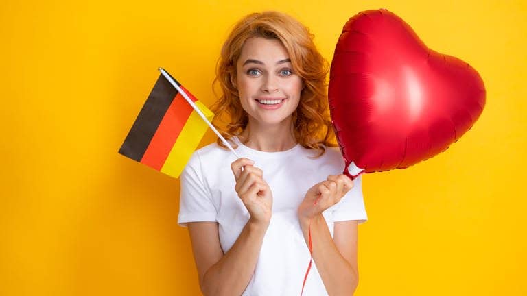 Eine Frau hält eine Flagge von Deutschland und ein rotes Luftballonherz. Sie lacht glücklich.
