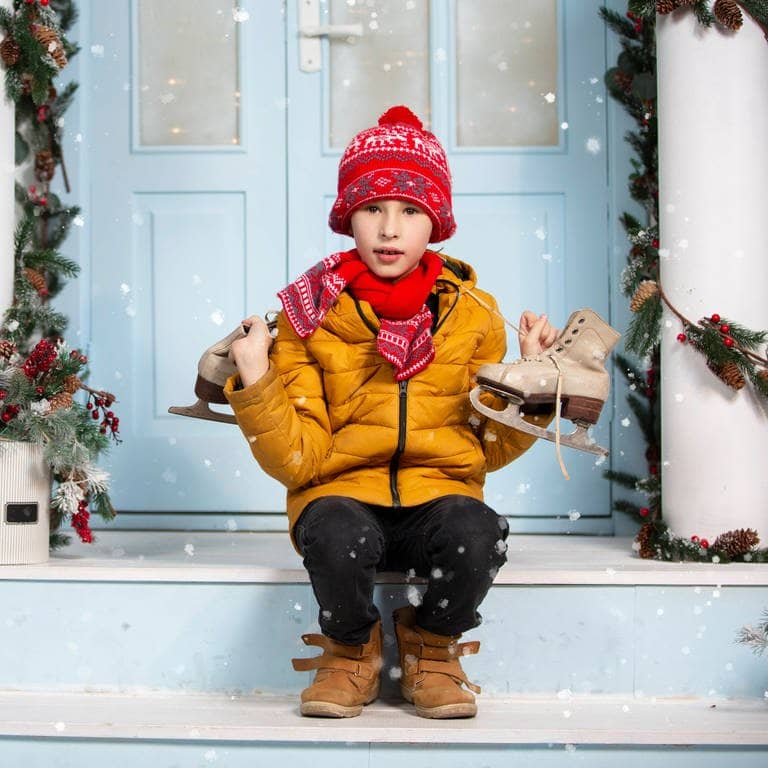 Weiße Weihnachten 2023? Junge sitzt mit Schlittschuhen auf der Treppe vor einer Haustür, Schnee fällt vom Himmel und es ist klassisch Winter. (Foto: IMAGO, IMAGO / Zoonar)