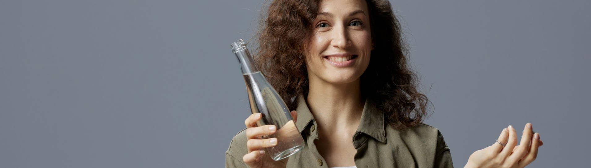 Frau hält ein Glas mit Leitungswasser in der Hand und fragt sich, welche Mythen stimmen.