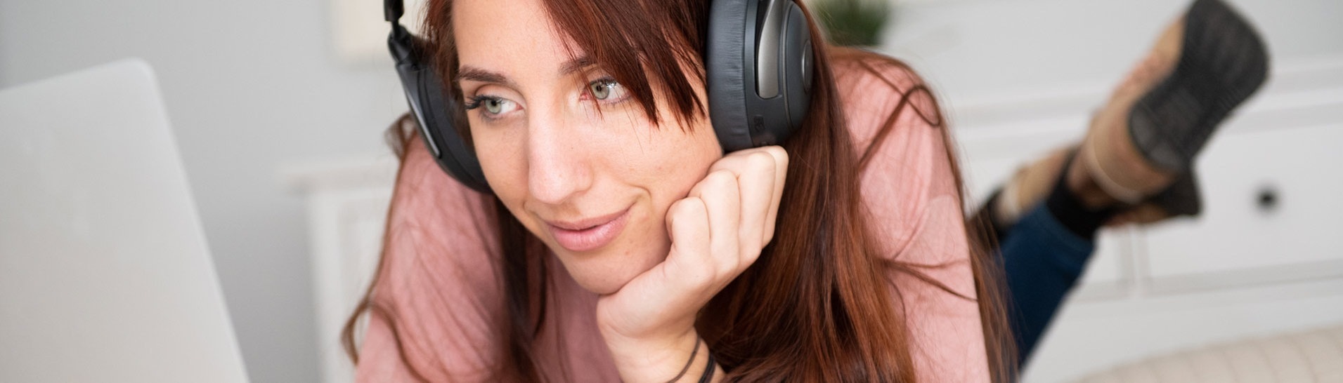 Eine Frau liegt auf dem Bett und schaut mit Kopfhörern auf den Ohren am Laptop eine Serie (Foto: picture-alliance / Reportdienste, picture alliance / dpa Themendienst | Franziska Gabbert)