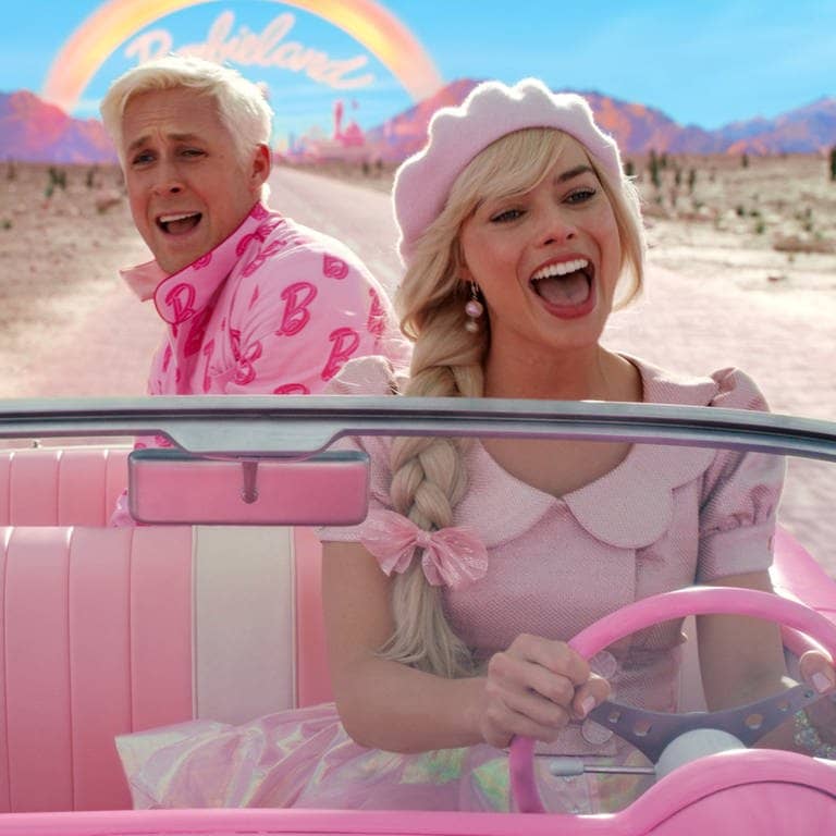 Ryan Gosling als Ken und Margot Robbie als Barbie in einer Szene des Barbie-Films. Die Hauptdarsteller fahren mit einem Auto aus Barbieland heraus. (Foto: dpa Bildfunk, picture alliance/dpa/Warner Bros. Entertainment | -)