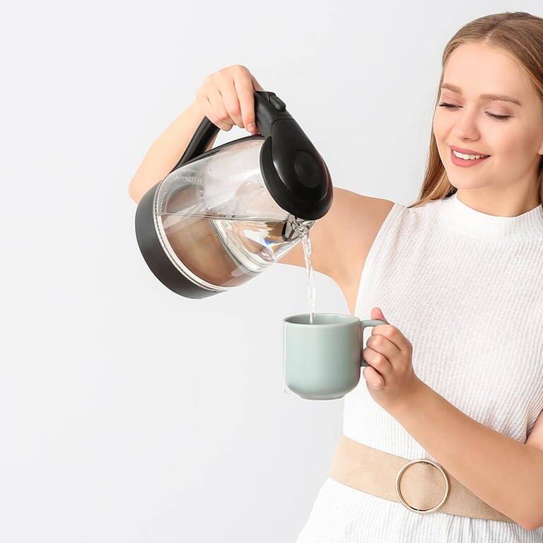 Frau schenkt sich aus dem Wasserkocher Wasser in eine Tasse ein (Foto: Adobe Stock / Pixel-Shot)