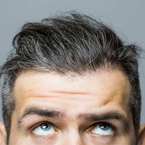 Mann schaut besorgt auf sein grau werdendes Haar  (Foto: Adobe Stock/Volodymyr)