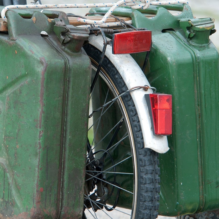 Zwei grüne Benzinkanister, die an einem Fahrradgepäckträger hängen.