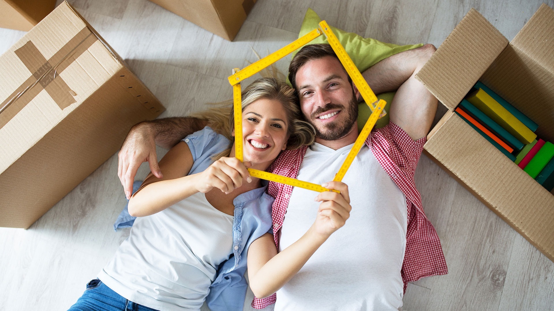 Mann und Frau liegen auf dem Boden, zwoschen Umzugskisten und lächeln in die Kamera  (Foto: Adobe Stock / didesign)