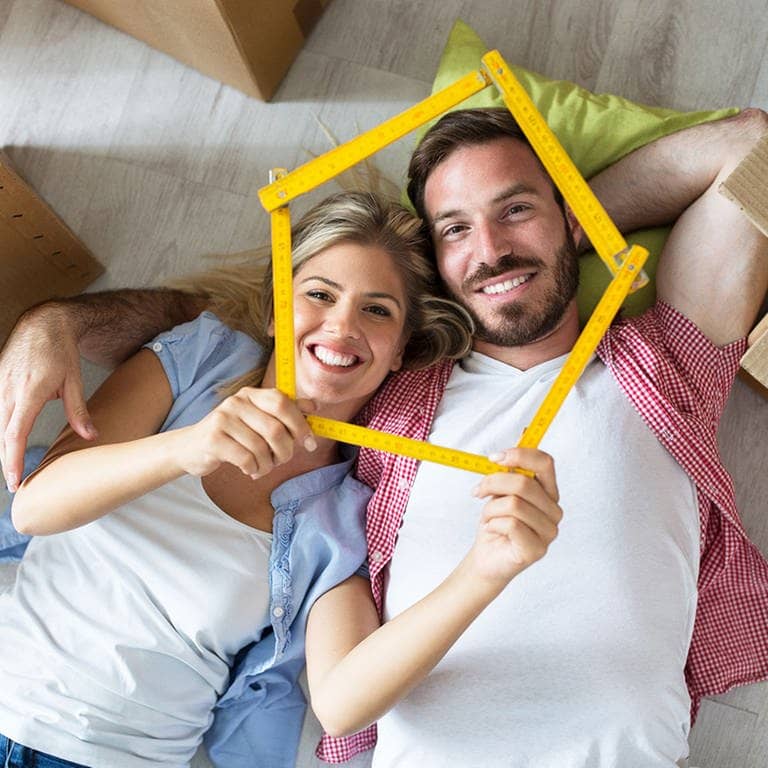 Mann und Frau liegen auf dem Boden, zwoschen Umzugskisten und lächeln in die Kamera  (Foto: Adobe Stock / didesign)
