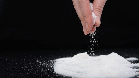 Hand die eine Prise Salz auf eine schwarze Flaeche streut 