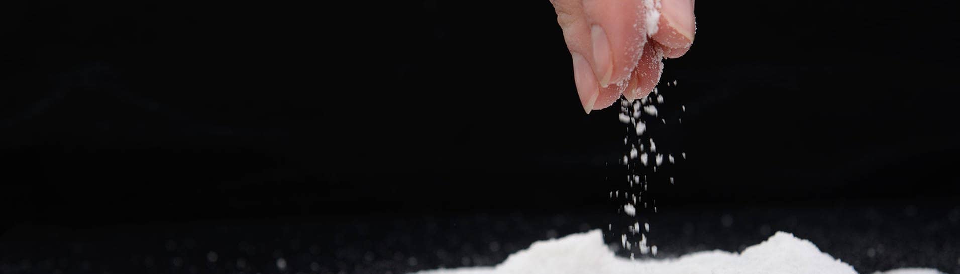 Hand die eine Prise Salz auf eine schwarze Flaeche streut  (Foto: Adobe Stock / yuryastankov)