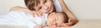 Älterer Bruder umarmt neugeborenes Baby