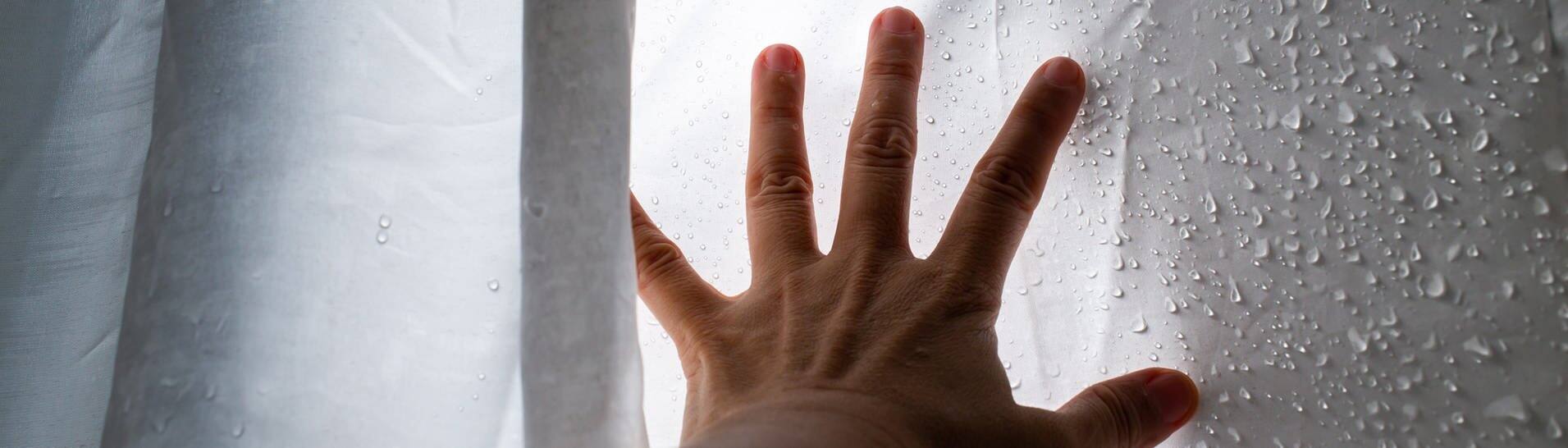 Hand am nassen Duschvorhang (Foto: Adobe Stock/eyepark)