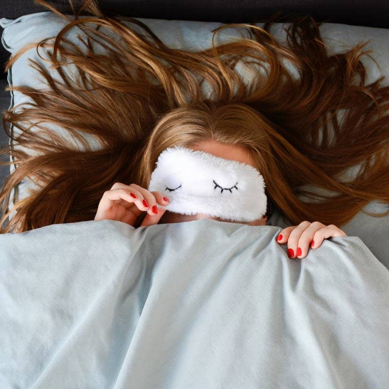 Junge Frau mit langen Haaren und Schlafmaske liegt im Bett (Foto: Adobe Stock/Evelien)