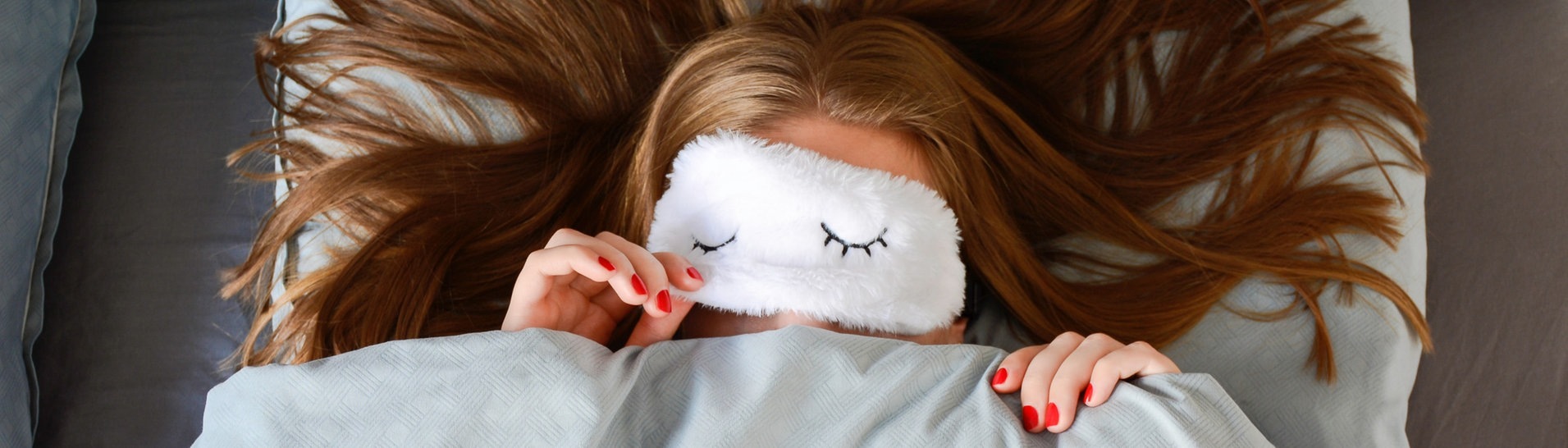 Junge Frau mit langen Haaren und Schlafmaske liegt im Bett (Foto: Adobe Stock/Evelien)