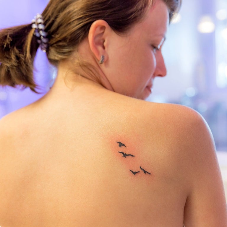 Frisches Tattoo mit fliegenden Vögeln auf dem Rücken einer jungen Frau (Foto: Adobe Stock/Mariakray)