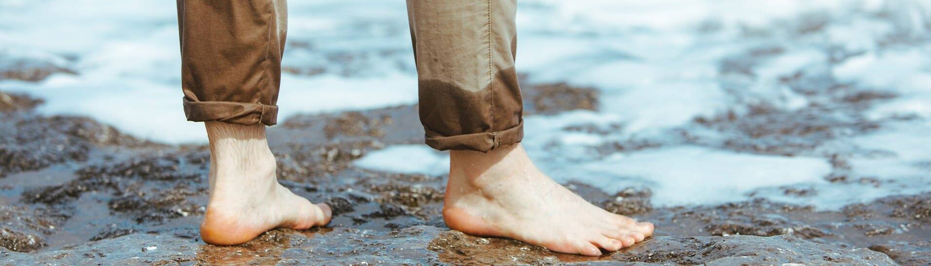 Mann mit halbnassen Hosenbeinen steht im Wasser (Foto: Adobe Stock, phpetrunina14)