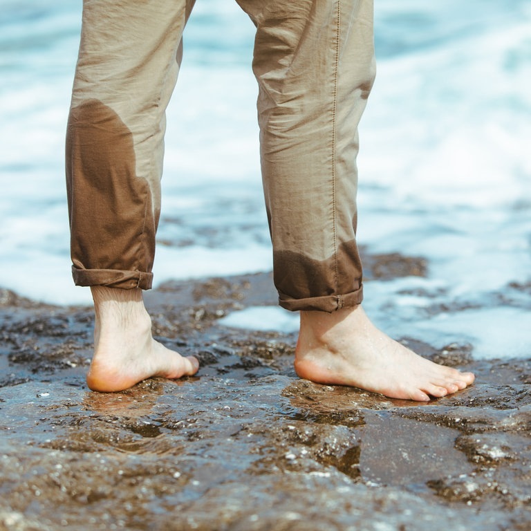 Mann mit halbnassen Hosenbeinen steht im Wasser (Foto: Adobe Stock, phpetrunina14)