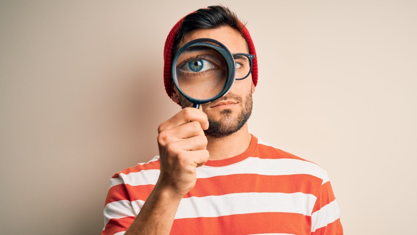 Mann mit ernstem Blick schaut durch eine Lupe (Foto: Adobe Stock, Krakenimages.com)