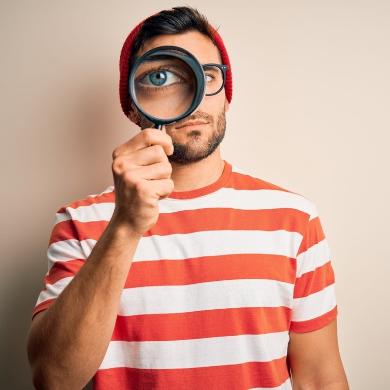 Mann mit ernstem Blick schaut durch eine Lupe (Foto: Adobe Stock, Krakenimages.com)