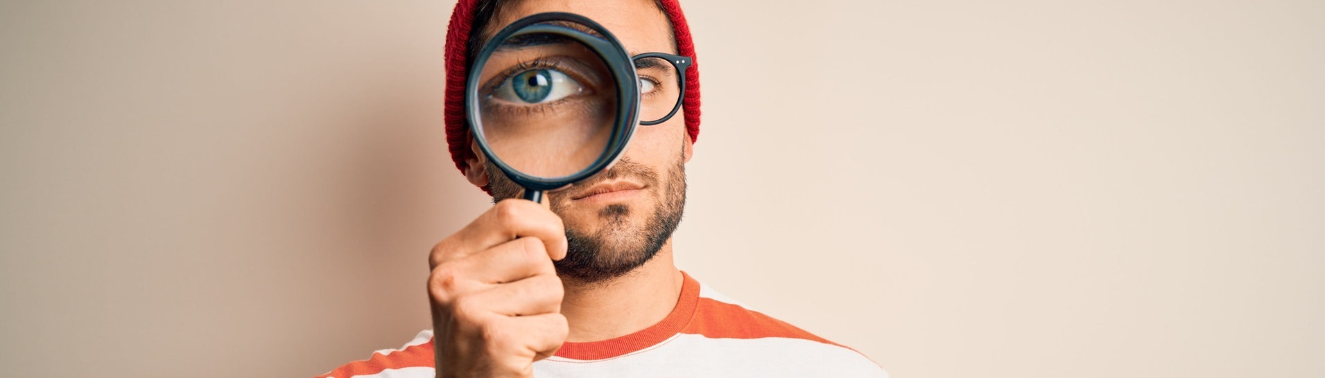 Mann mit ernstem Blick schaut durch eine Lupe (Foto: Adobe Stock, Krakenimages.com)