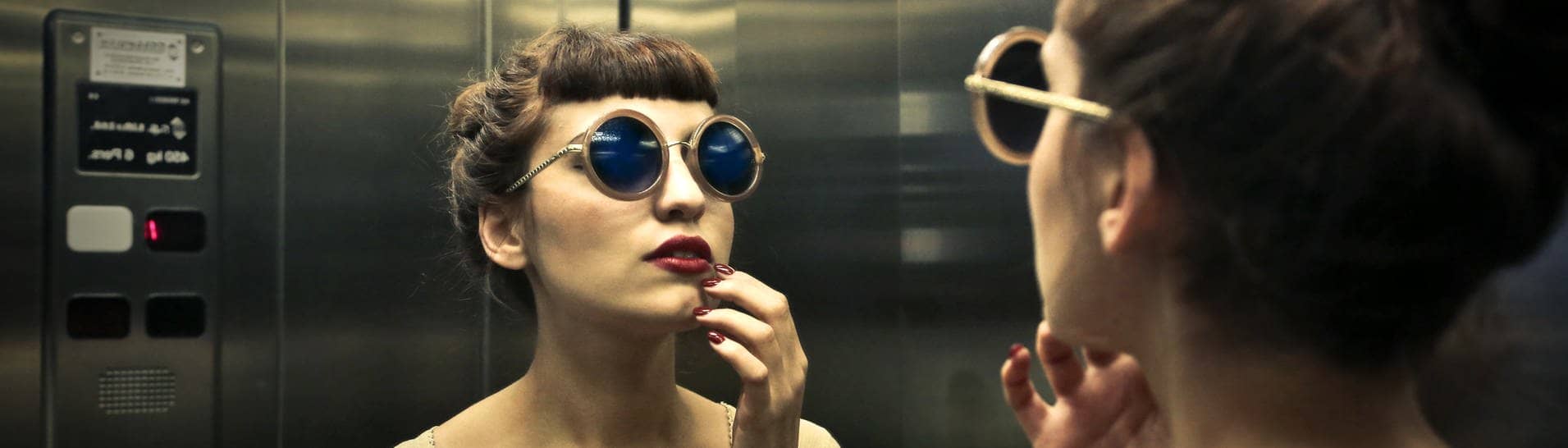Frau betrachtet sich im Spiegel des Aufzugs (Foto: Adobe Stock, olly)