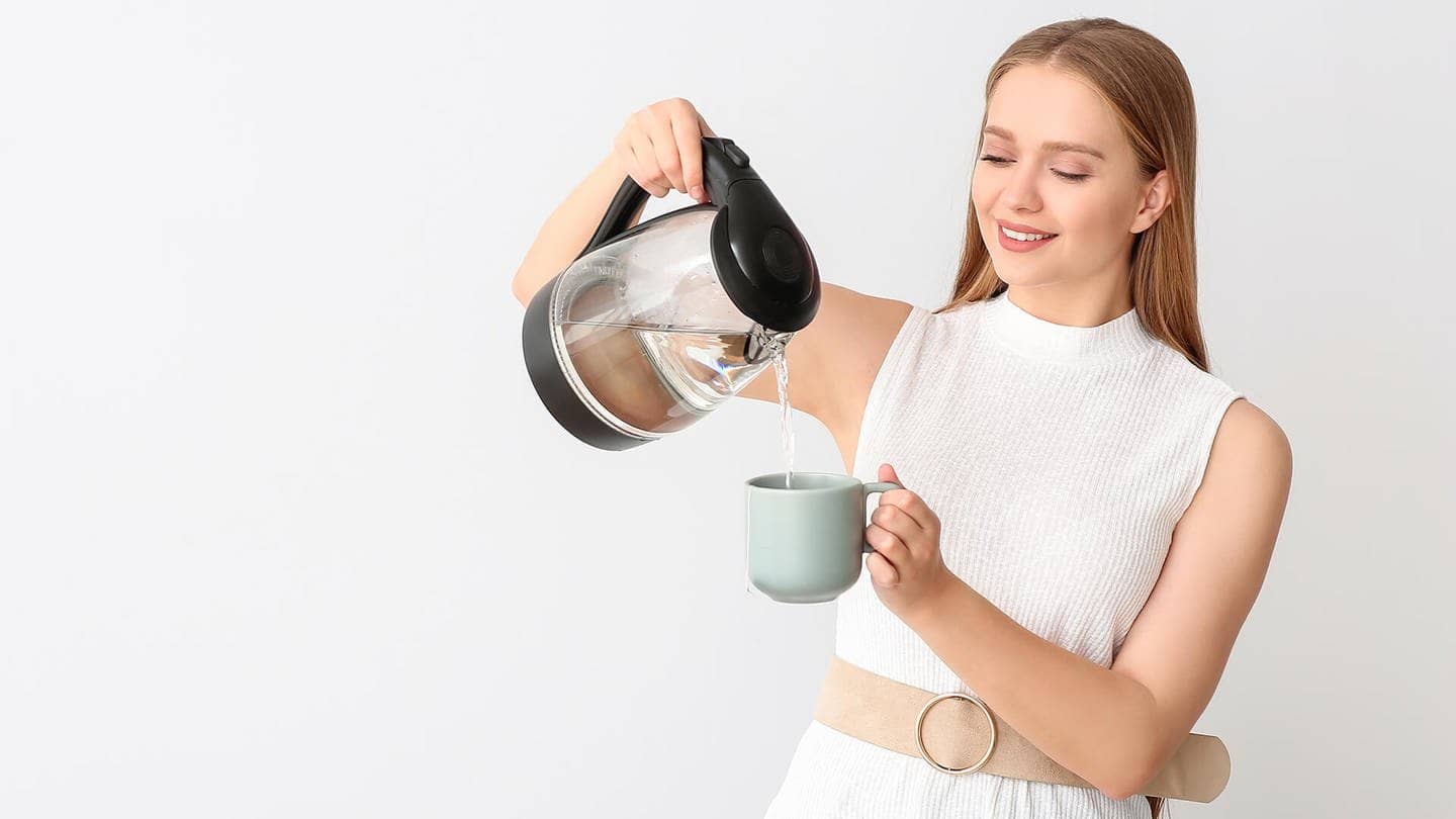 Frau schenkt sich aus dem Wasserkocher Wasser in eine Tasse ein