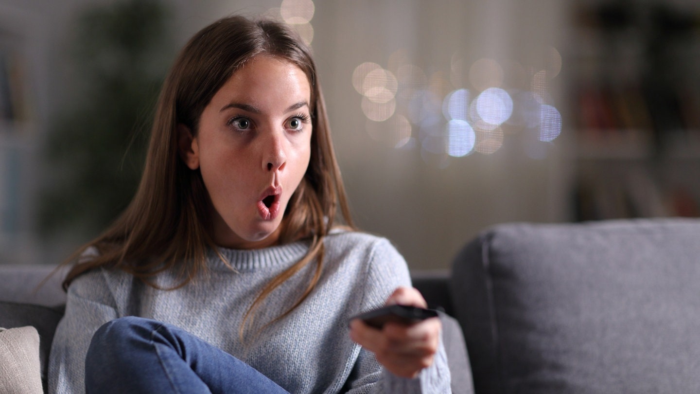 Überrraschte Frau beim Frensehen zu Hause auf dem Sofa