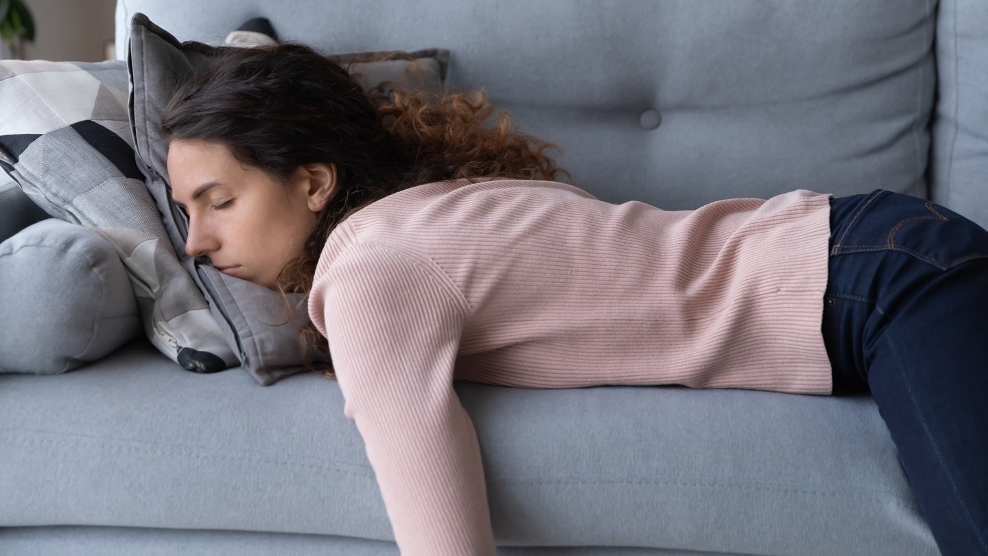 Junge Frau schläft erschöpft auf dem Sofa (Foto: Adobe Stock,  fizkes)