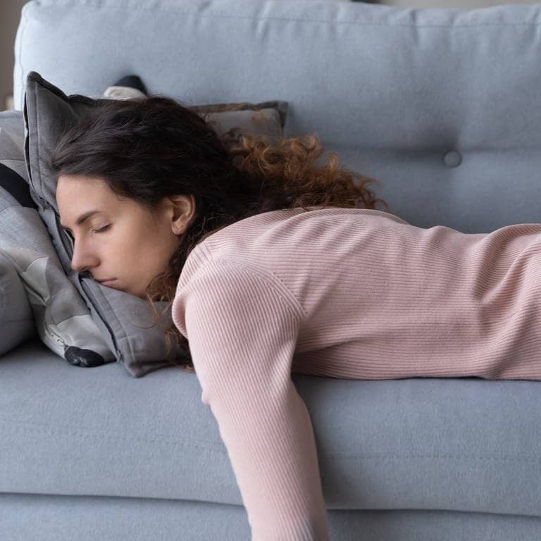 Junge Frau schläft erschöpft auf dem Sofa