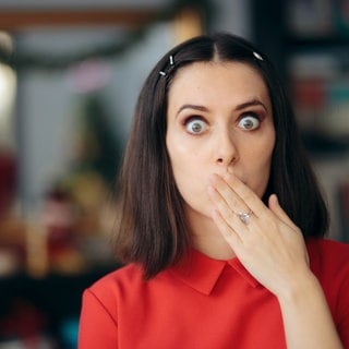 Frau mit erschrockenem Blick hält sich den Mund zu