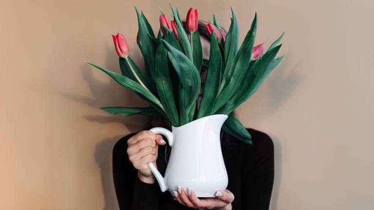 Eine Frau hält rote Tulpen in einer Vase vor ihr Gesicht, das Menschen mit Rot-Grün-Schwäche nicht so deutliche erkennen werden