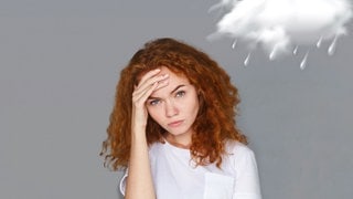 Eine junge Frau hat Kopfschmerzen wegen des Wetterumschwungs.Mit schmerzverzerrtem Gesicht hält sich die Hand an die Stirn. Über ihr schwebt eine Regenwolke.