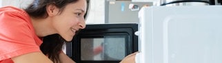 Eine Frau greift in die Mikrowelle und entnimmt ihr Essen.