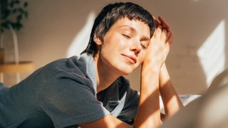 Eine Frau liegt vorm Fenster und genießt die Sonne, die auf ihr Gesicht fällt, sie fragt sich, ob sie auch hinter der Fensterscheibe einen Sonnenbrand bekommen kann. (Foto: Adobe Stock, Ilona) Eine Frau liegt vorm Fenster und genießt die Sonne, die auf ihr Gesicht fällt, sie fragt sich, ob sie auch hinter der Fensterscheibe einen Sonnenbrand bekommen kann.