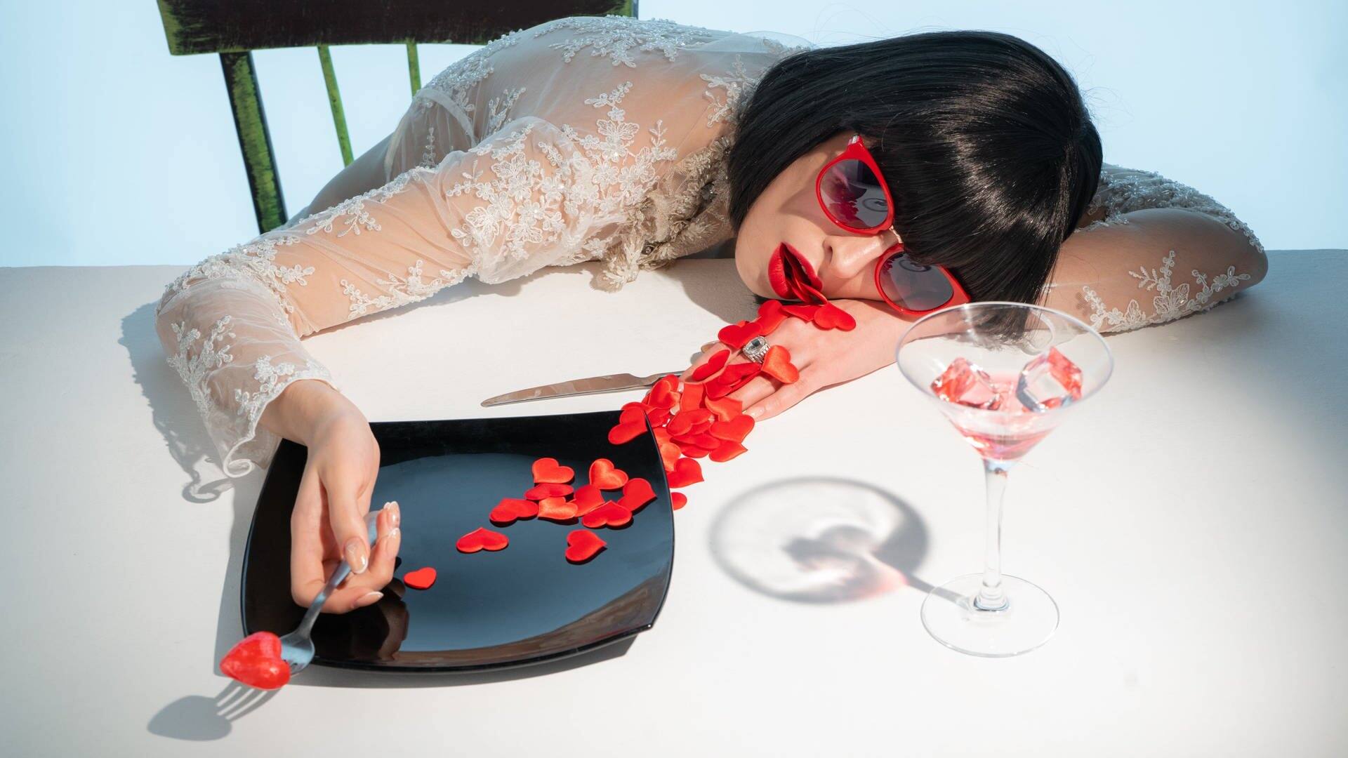 Una mujer se acuesta en una mesa de comedor y se atraganta con los corazones que salen de su boca (Foto: Adobe Stock/razoomanetu)
