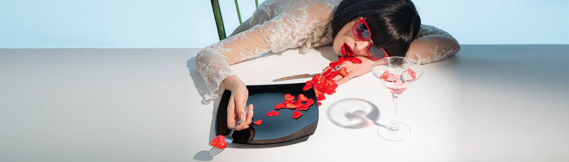 Frau liegt auf dem Esstisch – erstickt an Herzen, die ihr aus dem Mund quellen (Foto: Adobe Stock/razoomanetu)