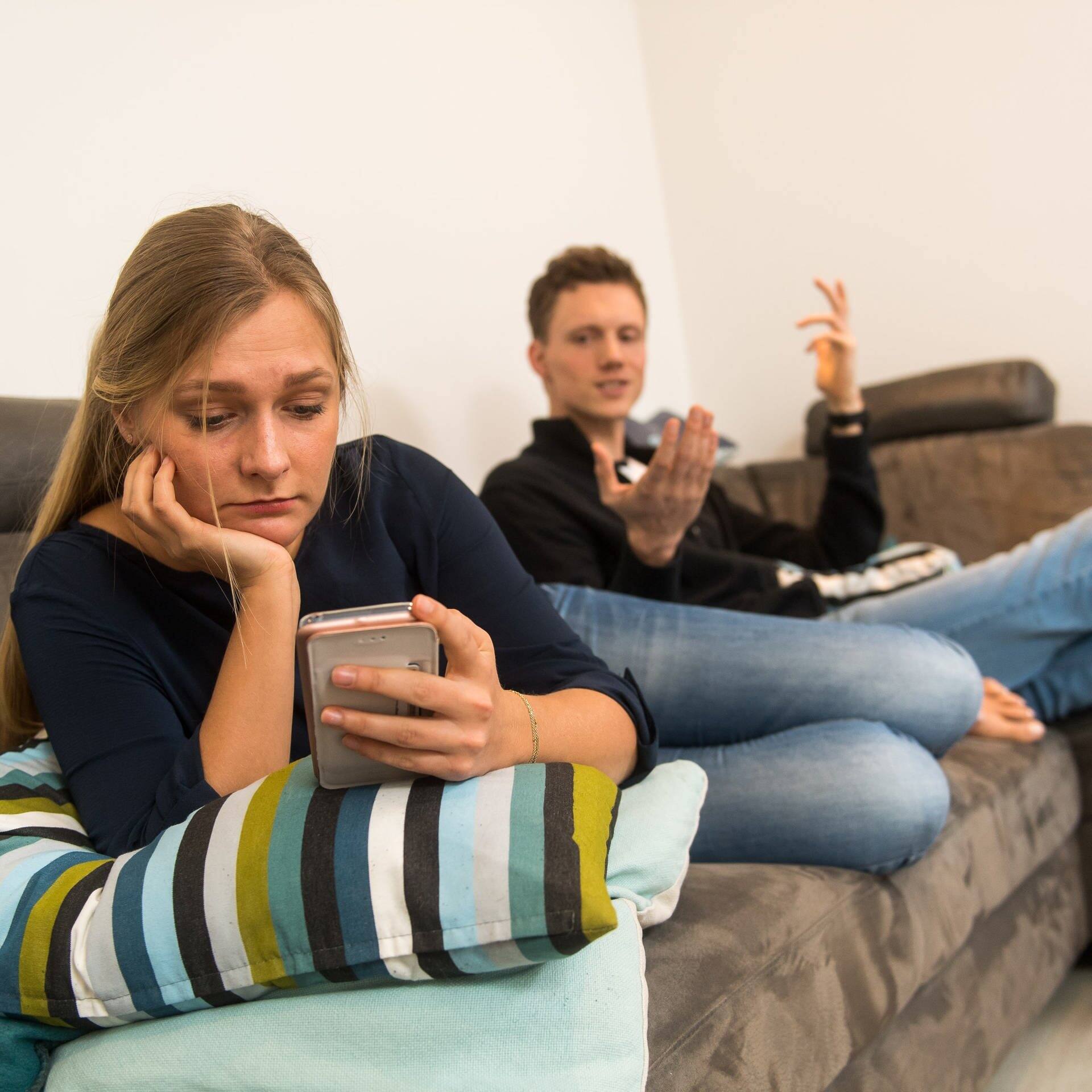 Ein Paar streitet sich auf einem Sofa, weil sie ihm zu oft am Smartphone ist. (Foto: picture-alliance / Reportdienste, picture alliance / dpa-tmn | Benjamin Nolte)