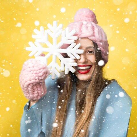 Junge Frau mit Handschuhen und Mütze, hält eine Schneeflocke hoch und lacht (Foto: Adobe Stock/rh2010)