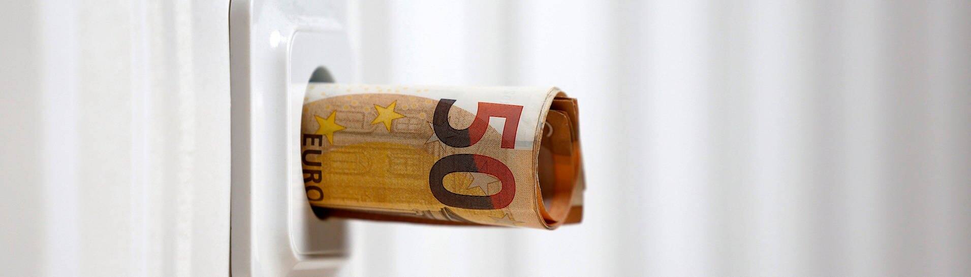 Symbolbild für die Energiekrise: Zusammengerollte Geldscheine ragen aus einer Steckdose.  (Foto: IMAGO, IMAGO / Panama Pictures)