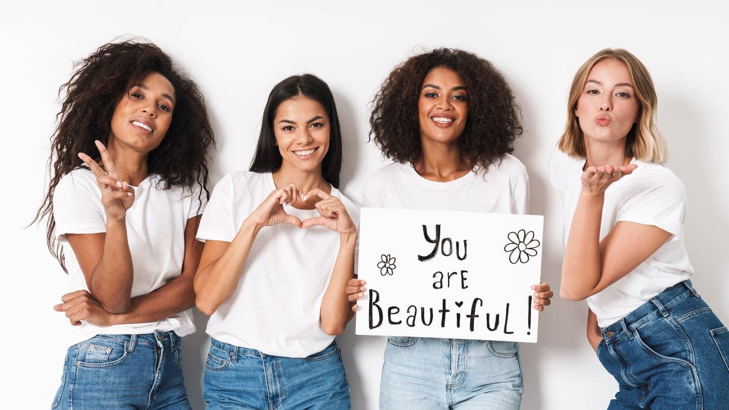 Vier junge Frauen, eine hält ein Schild mit der Aufschrift "Du bist schön", die anderen formen mit ihren Händen Herzen (Foto: Adobe Stock, Adobe Stock/Drobot Dean)