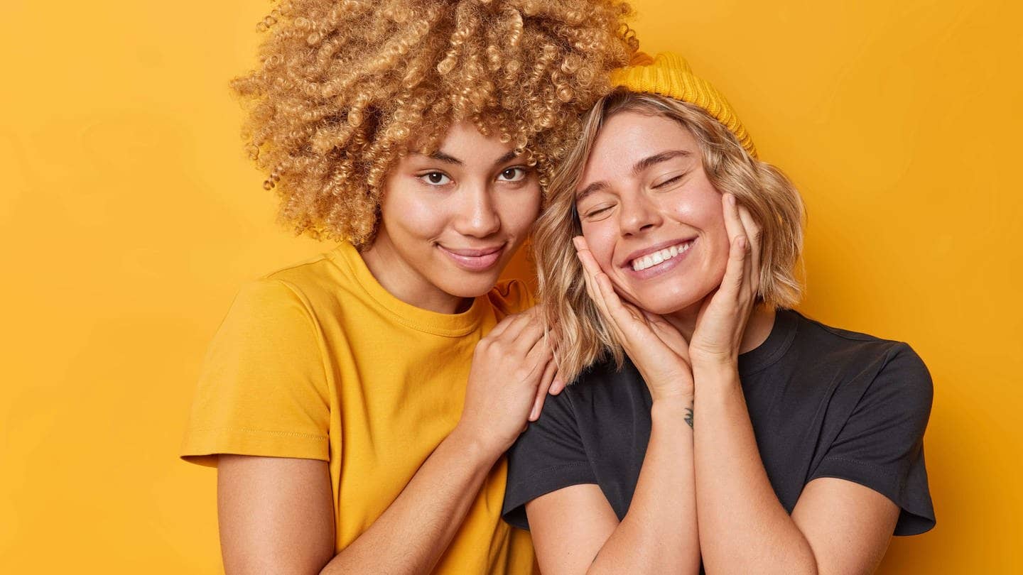 Zwei junge Frauen vor gelbem Hintergrund lächeln, eine hält der anderen die Schulter, die andere schlägt die Hände glücklich übers Gesicht (Foto: Adobe Stock, Adobe Stock / Wayhome Studio)