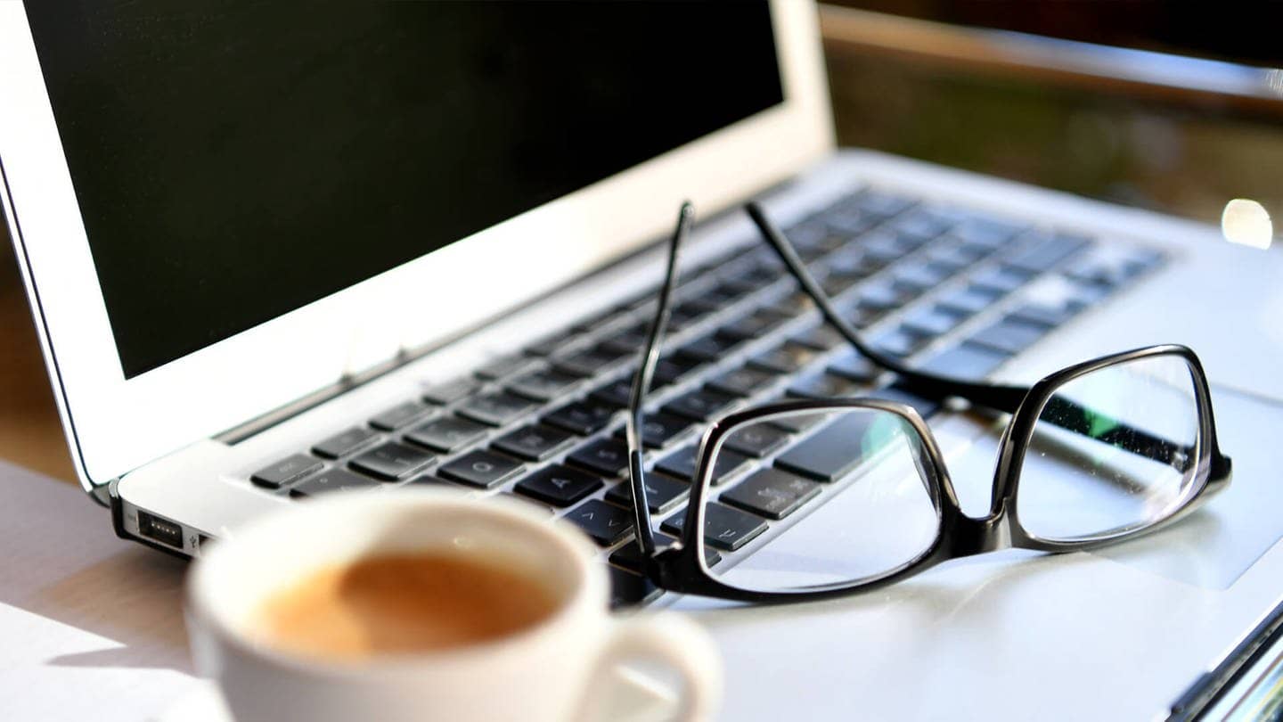 Brille auf Laptop und Kaffeetasse