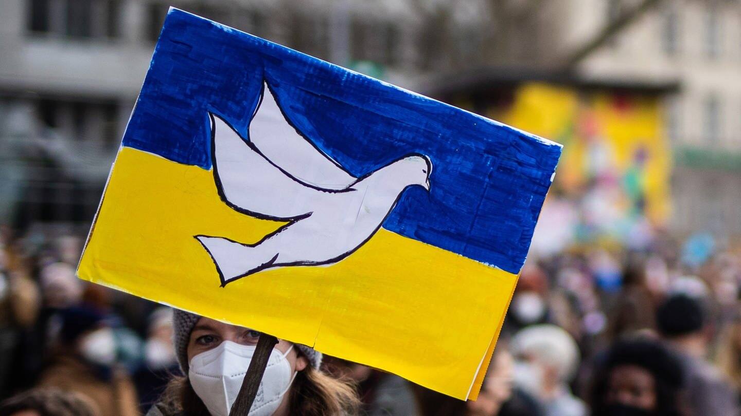 Bei einer Demonstration gegen den militärischen Einsatz Russlands in der Ukraine hält eine Frau in Schild mit den Farben der Ukrainischen Flagge und einer Friedenstaube darauf in ihrer Hand. (Foto: dpa Bildfunk, picture alliance/dpa | Christoph Schmidt)