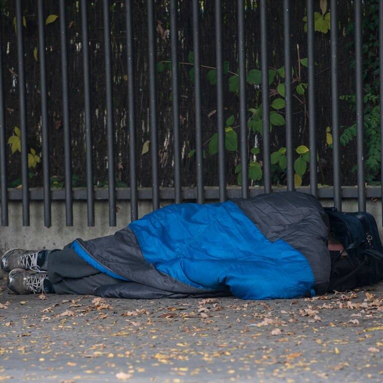 Ein Obdachloser liegt in einem Schlafsack gehüllt auf der Straße (Symbolbild)