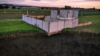Ein halbfertiges Haus ist am Rande eines großen mit Wasser gefüllten Kraters zu sehen. (Foto: dpa Bildfunk, picture alliance/dpa | Karlos Pin-Punk) Ein halbfertiges Haus ist am Rande eines großen mit Wasser gefüllten Kraters zu sehen.