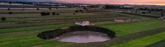 Auf einem Feld ist ein großer mit Wasser gefüllter Krater zu sehen. 