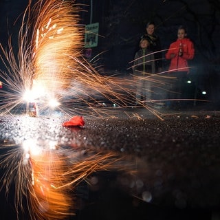 Mehrere Personen sehen einem funkensprühenden Bodenfeuerwerk zu.