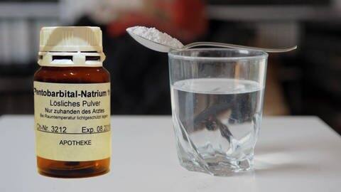 Eine Flasche Natrium-Pentobarbital, daneben ein Wasserglas mit einem Löffel, auf dem Pulver gehäuft ist (Foto: IMAGO, imago images/sepp spiegl)