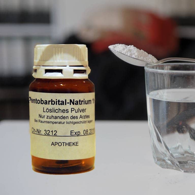 Eine Flasche Natrium-Pentobarbital, daneben ein Wasserglas mit einem Löffel, auf dem Pulver gehäuft ist (Foto: IMAGO, imago images/sepp spiegl)