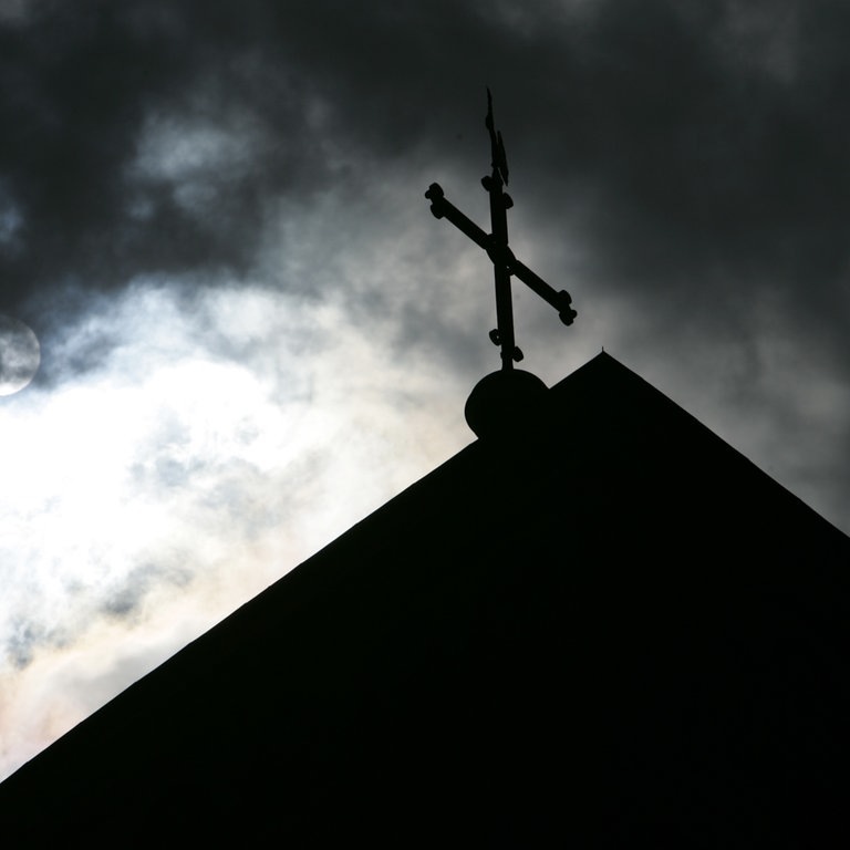 Im Gegenlicht und vor wolkenverhangenem Himmel ist die Kirchturmspitze des Doms in Osnarbrück mit Kreuz zu sehen. (Foto: dpa Bildfunk, picture alliance/dpa | Friso Gentsch)