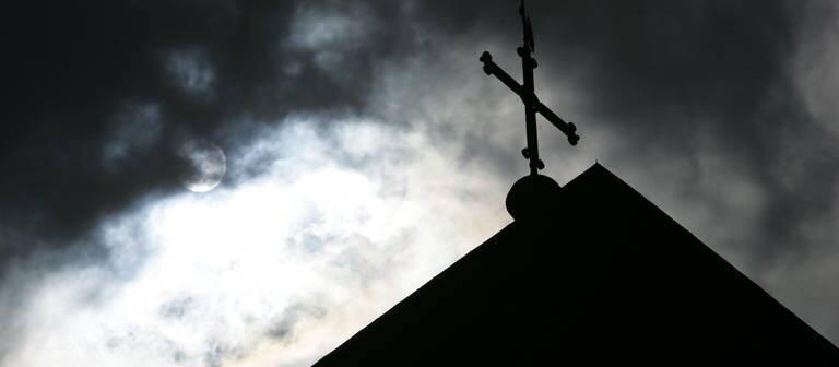 Im Gegenlicht und vor wolkenverhangenem Himmel ist die Kirchturmspitze des Doms in Osnarbrück mit Kreuz zu sehen. (Foto: dpa Bildfunk, picture alliance/dpa | Friso Gentsch)